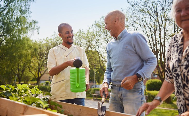 Tre personer står i trädgården utanför Bäckgården. En man är personal, en man är boende. Han håller i en planteringsspade och håller på att plantera.